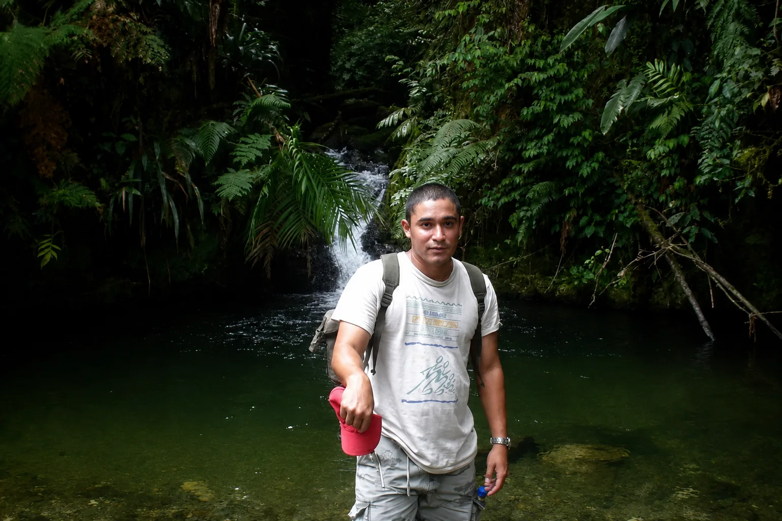 Abel Batista en un arroyo de bosque nublado, con una cascada detrás