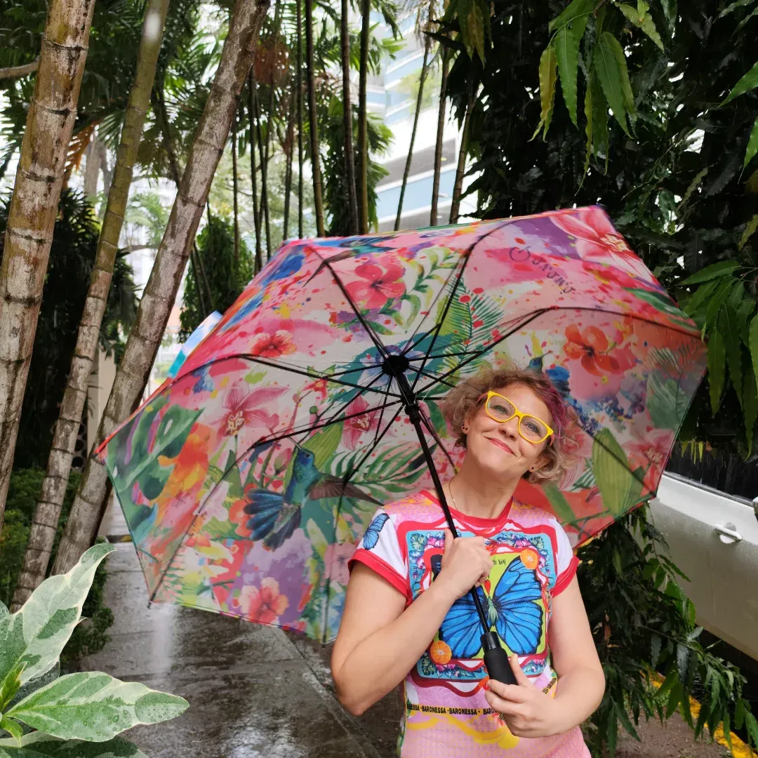 Serena Rinaudo bajo un paraguas con su estampado de colibríes, en un jardín tropical