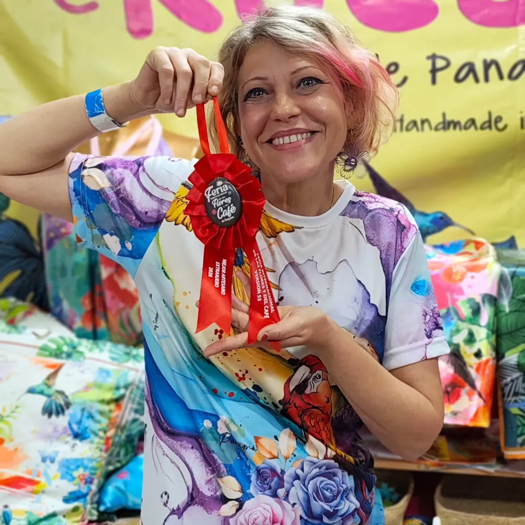 Serena Rinaudo, sonriente, muestra la escarapela roja de la Feria de las Flores y del Café de Boquete, con una camiseta de su propio estampado