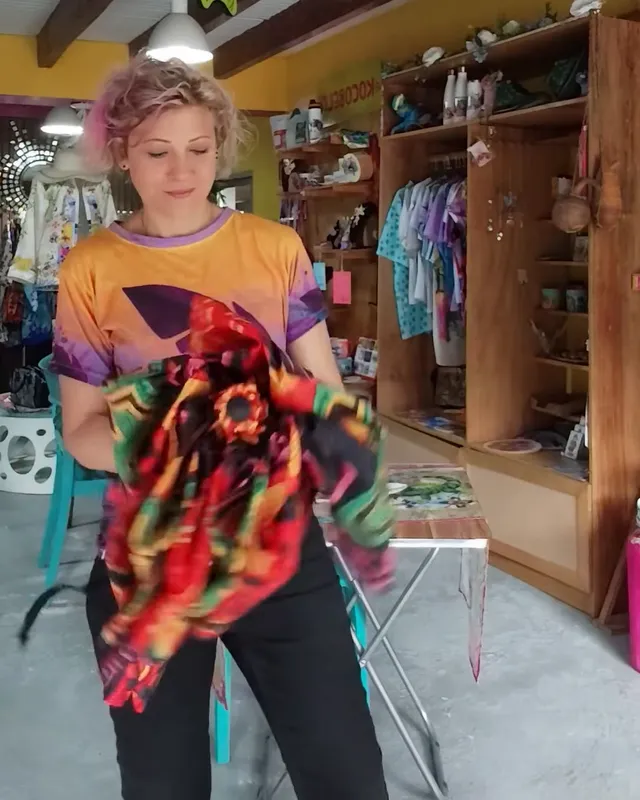 Serena dentro de la tienda de Boquete doblando un pañuelo de colores, con estantes de madera llenos de piezas detrás